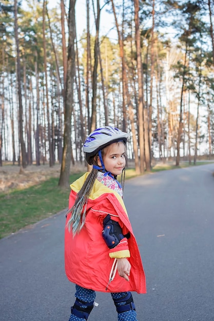 Glückliches Kind im Sporthelm, der auf Rollschuhen am Park reitet