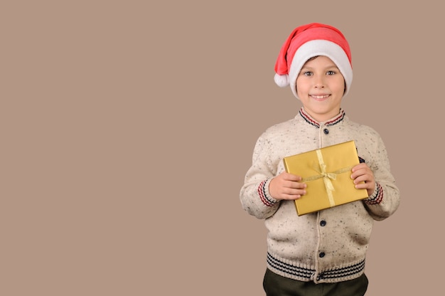 Glückliches Kind im Weihnachtsmann-Hut, der goldene Geschenkbox hält