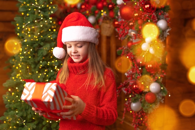 Glückliches Kind in einem roten Hut von Santa hält Weihnachtsgeschenk mit Lächeln. Weihnachtskonzept.