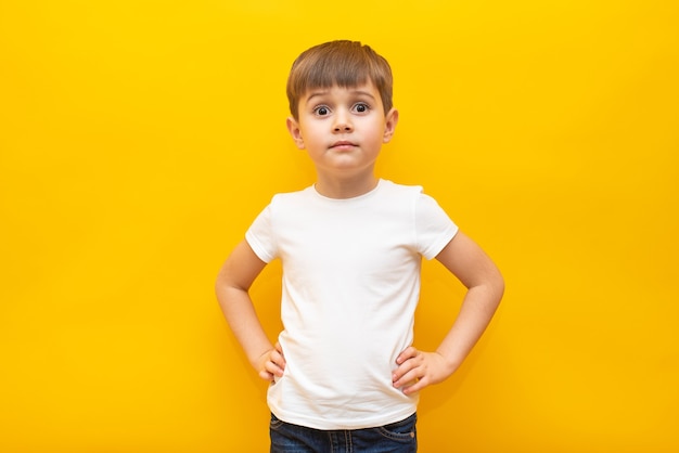 Glückliches Kind in einem weißen T-Shirt hält seine Hände am Gürtel an einer isolierten gelben Wand