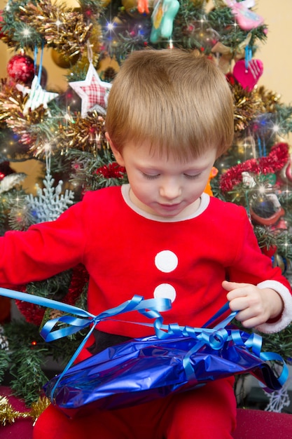 Glückliches Kind in Santa Claus, die offenes Weihnachtsgeschenk trägt