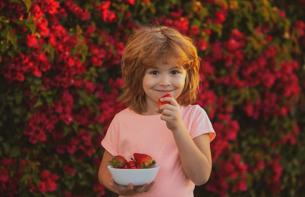 Glückliches Kind isst Erdbeeren im Sommer im Freien