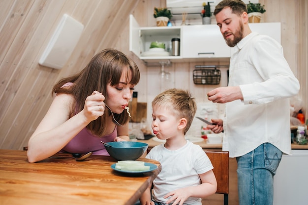 Glückliches Kind isst Nudeln in der Küche mit ihrer Familie