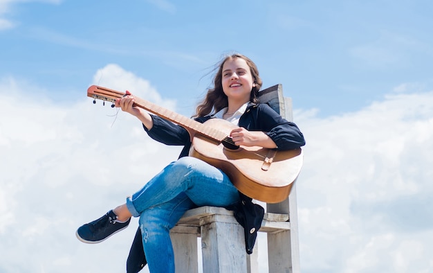 Glückliches Kind mit Akustikgitarre auf Himmelshintergrund, Musik.