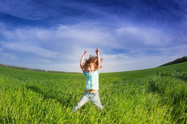 Glückliches Kind mit erhobenen Armen im grünen Frühlingsfeld gegen blauen Himmel Freiheits- und Glückskonzept