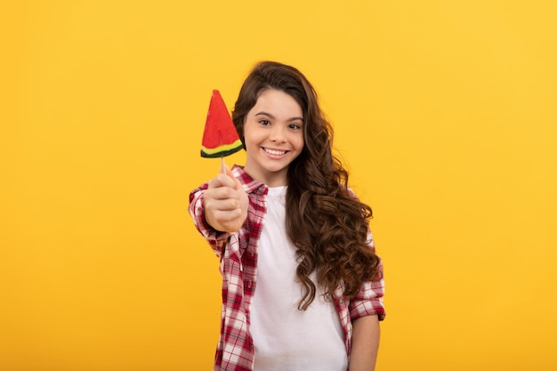 Glückliches Kind mit langen lockigen Haaren im karierten Hemd zeigt Lollipop-Karamellbonbons auf gelbem Hintergrund Zahnpflege