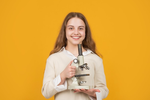 Glückliches Kind mit Mikroskop auf gelbem Hintergrund