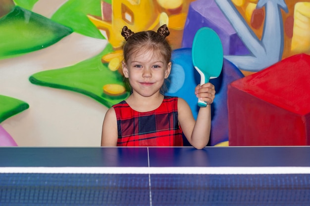 Glückliches Kind mit Tischtennisschläger im Spielzimmer