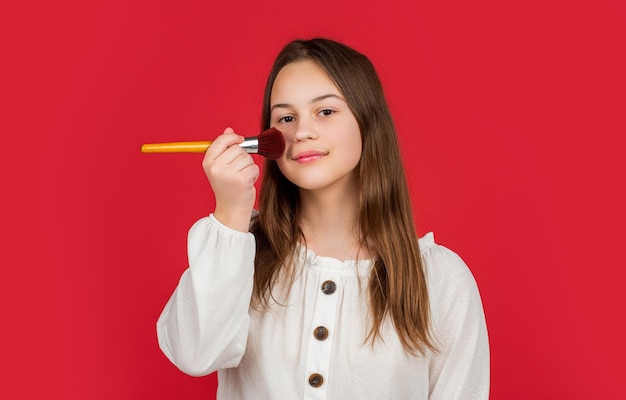 Glückliches Kind trägt mit Make-up-Pinsel Puder auf das Gesicht auf