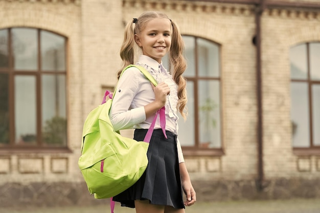 Glückliches Kind trägt Schultasche in formeller Modeuniform im Freien zurück zur Schule