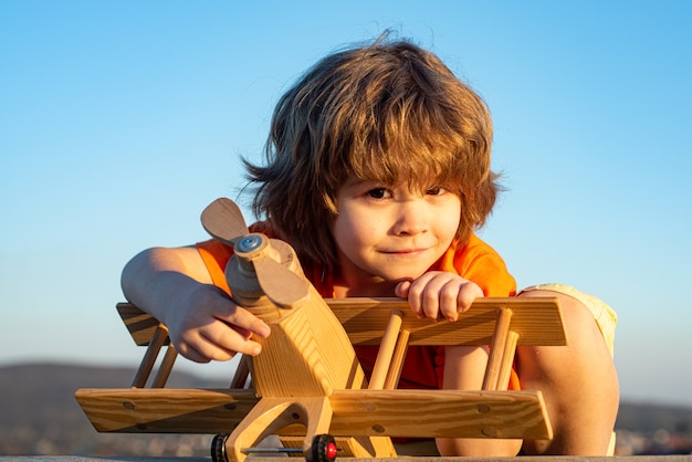 Glückliches Kind träumt vom Reisen und Spielen mit Spielzeugflugzeug. Kleiner Pilotflieger im Freien gegen blauen Sommerhimmelhintergrund. Kinderträume.