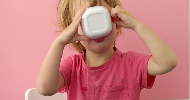 Glückliches Kind trinkt Milch von einer Schale auf Rosa