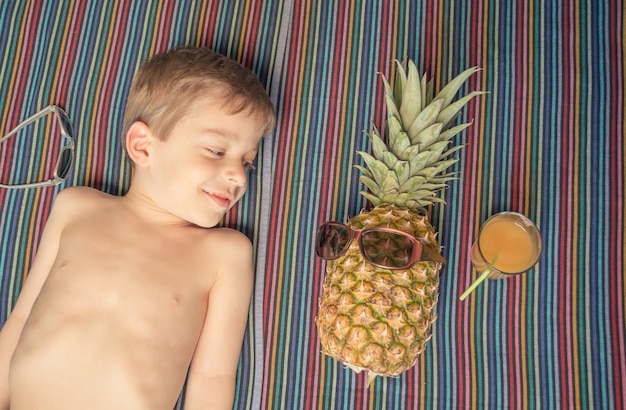Glückliches Kind und Ananas beim Sonnenbaden über einem Handtuch