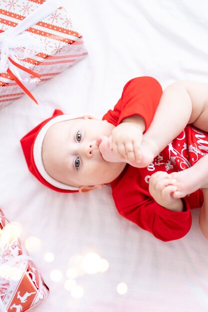 Glückliches Kinderbaby im roten Weihnachtskostüm, das zu Hause neues Jahr mit Geschenkennahaufnahmeporträt feiert