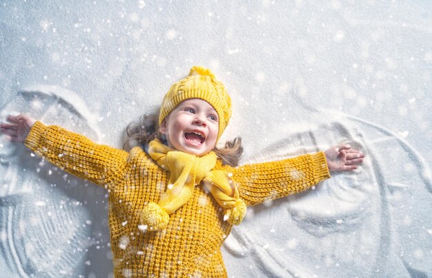 Glückliches Kindermädchen, das auf einem Winterspaziergang in der Natur spielt. Kind macht Schneeengel.