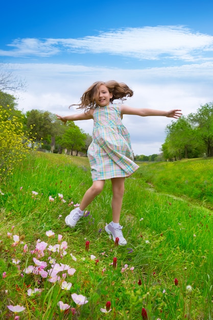 glückliches Kindermädchen, das auf Frühlingsmohnblumenblumen springt