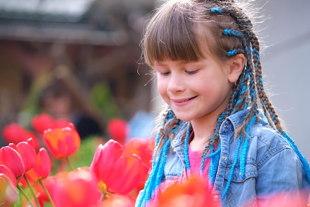 Glückliches Kindermädchen, das im Sommergarten den süßen Duft roter Tulpenblumen genießt