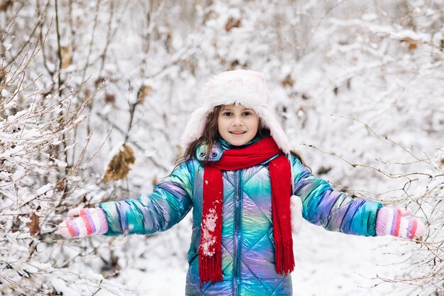 Glückliches Kindermädchen, das mit Schnee auf schneebedecktem Winterweg spielt.