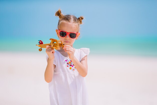 Glückliches Kindermädchen, das mit Spielzeugflugzeug am Strand spielt. Kinder träumen davon, Pilot zu werden