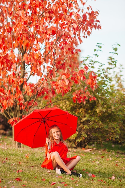 Glückliches kindermädchen lacht unter rotem regenschirm