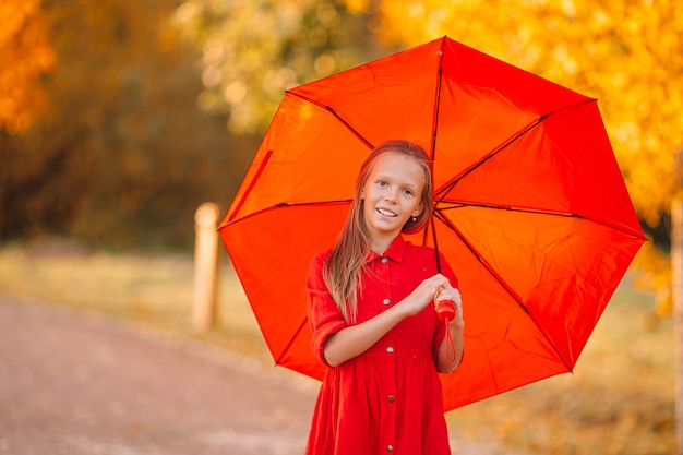 Glückliches Kindermädchen lacht unter rotem Regenschirm