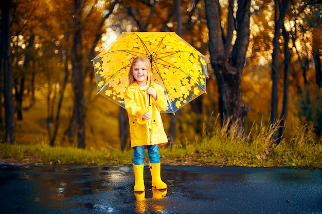 Glückliches Kindermädchen mit einem Regenschirm und Gummistiefeln ein Herbstweg