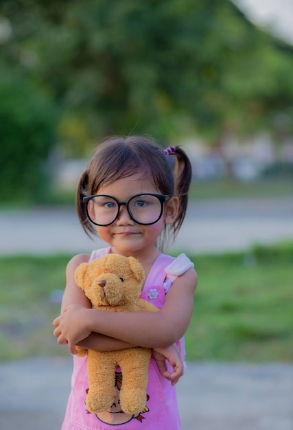 Glückliches Kindermädchen mit umarmendem Teddybär im Kleid im Sommergarten im Freien