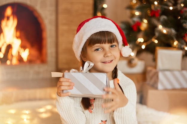 Glückliches Kindermädchen mit Weihnachtsgeschenk, das direkt in die Kamera schaut