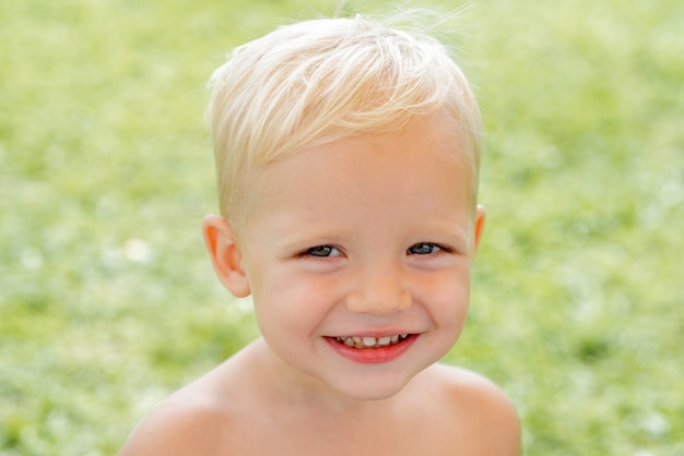 Glückliches Kinderporträt lustiger Junge glücklicher Junge, der am sonnigen Sommertag glücklichen Tag im Gras steht