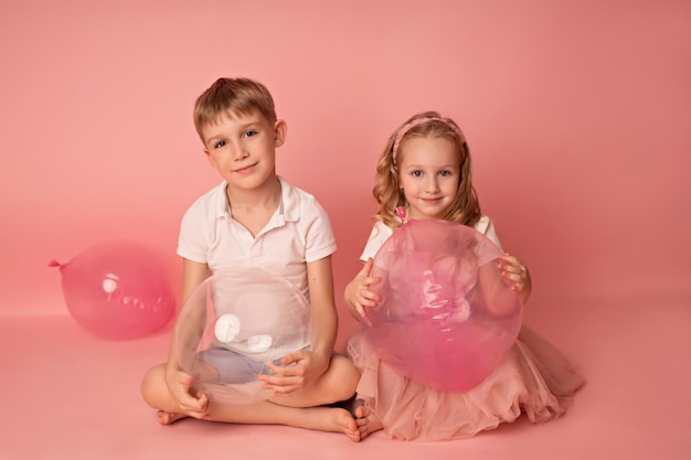 Glückliches Kindmädchen und -junge auf einem rosa Hintergrund mit Luftballons. Feier. Geburtstag