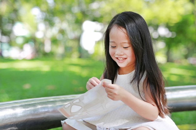 Glückliches kleines asiatisches Kindermädchen, das Aufkleber im grünen Park spielt.