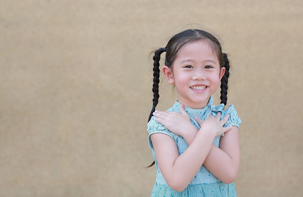 Glückliches kleines asiatisches Kindermädchenausdruckkreuz irgendjemandes Arm und Lächeln. Selbstbewusste und fröhliche Kinder.