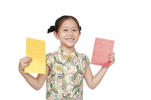 Glückliches kleines asiatisches Mädchen, das cheongsam lächelt und Gold- und Rotumschlag über weißem Hintergrund hält.