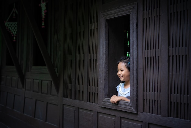 Glückliches kleines asiatisches Mädchen, das das Fenster bereitsteht