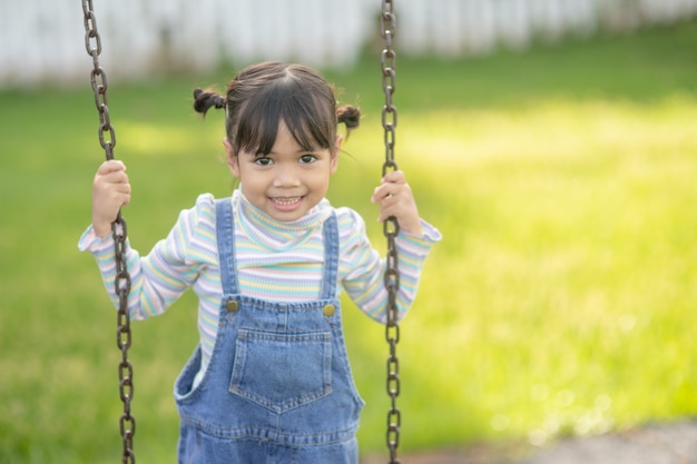 Glückliches kleines asiatisches Mädchen, das im Park im Freien Schaukel spielt