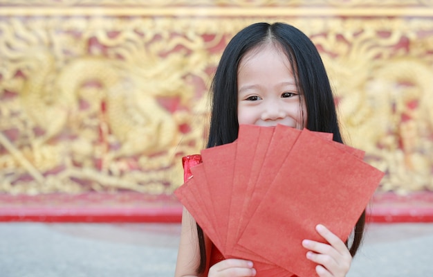 Glückliches kleines asiatisches Mädchen, das viele roten Umschläge hält. Feier des Chinesischen Neujahrsfests.