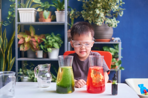 Glückliches kleines asiatisches schulkind, das wissenschaft studiert und diy lava lamp science experiment mit öl, wasser und lebensmittelfarbe macht