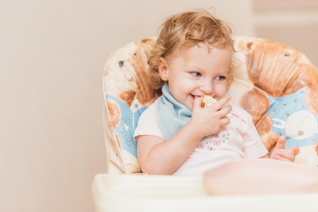 Glückliches kleines Baby isst zu Hause auf einem Stuhl sitzend