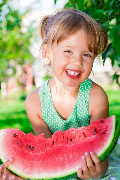 Glückliches kleines blondes Mädchen mit großer Scheibe Wassermelone in der Sommerzeit im Park, im Freien.