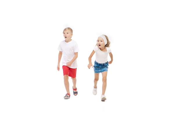 Glückliches kleines kaukasisches Mädchen und Junge, die isoliert auf weißem Hintergrund springen und laufen