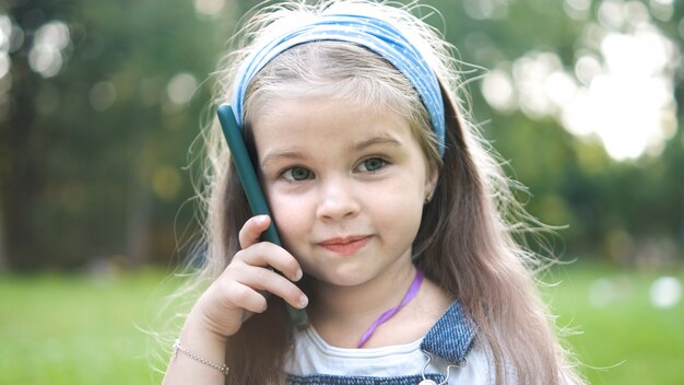 Glückliches kleines Kindermädchen, das Gespräch auf ihrem Sellphone im Sommerpark hat.