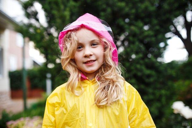 Glückliches kleines Kindermädchen im gelben Regenmantel.