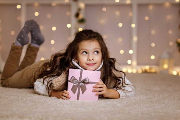 Glückliches kleines Kindermädchen mit Geschenkbox, die auf dem Boden sitzt