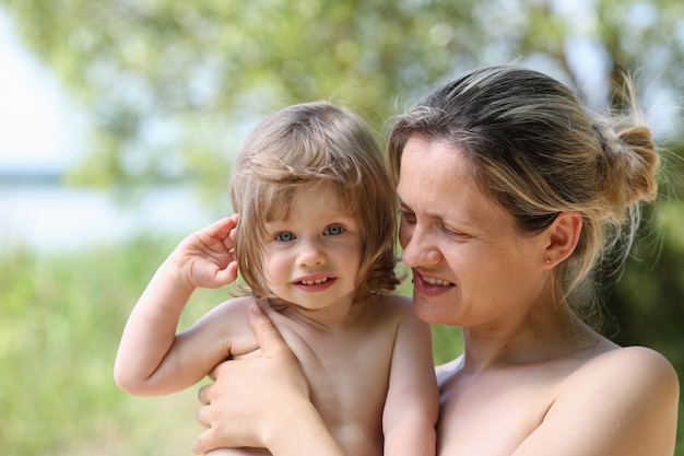 Glückliches kleines lächelndes Kind in den Armen der Mutter