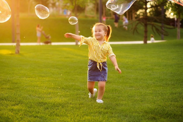 Glückliches kleines Mädchen 4-5 Jahre alt spielt mit Seifenblasen im Sommer im Park. Lebensstil der Kinder.