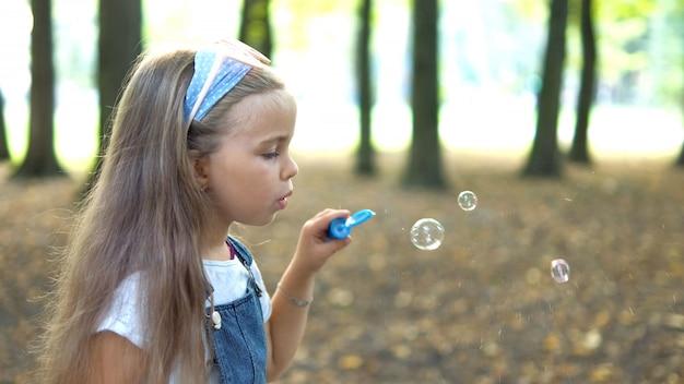 Glückliches kleines Mädchen bläst Seifenblasen draußen im grünen Park. Outdoor-Sommeraktivitäten für Kinderkonzept.