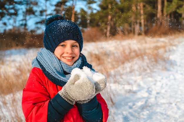 Glückliches kleines Mädchen, das im Winterwald am sonnigen Tag geht