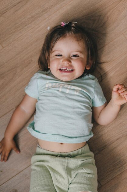 Glückliches kleines Mädchen, das in die Kamera lächelt, während es auf ihrem Bett auf dem Boden liegt Ansicht von oben Beauty-Konzept Familienkonzept Lächelndes Mädchen Relax-Konzept Kinderbetreuung