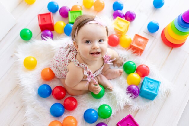 Glückliches kleines Mädchen, das in einem weißen Raum in einem roten Kleid mit hellen Spielzeugen sitzt und oben schaut