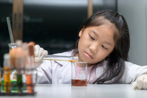 Glückliches kleines Mädchen, das Laborkittel macht, das Experiment macht